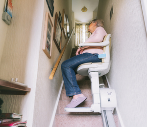 Senior woman using automatic stair lift on a staircase at her home. Medical Stairlift for disabled people and elderly people in the home. Selective focus.